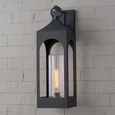 an outdoor light hanging on the side of a brick wall next to a white brick wall