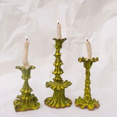 three green candlesticks sitting next to each other on a white tablecloth background