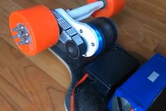 an orange and black skateboard with two wheels on top of wooden floor next to blue box