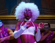 a woman with white hair is dancing in front of other people wearing purple and silver outfits