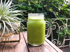 a green smoothie sitting on top of a wooden table next to a potted plant