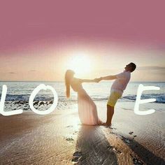 a man and woman standing on top of a beach next to the ocean holding hands