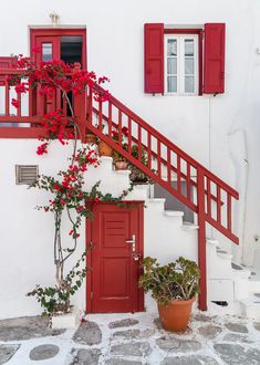 a red door and some plants on the side of a white building with red shutters