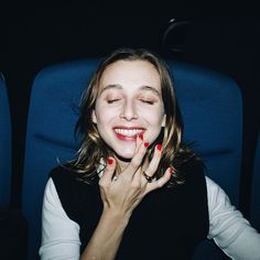 a woman sitting in an airplane seat with her hands on her face, smiling and looking at the camera