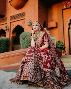 a woman in a red and gold bridal outfit sitting on the steps outside an orange building