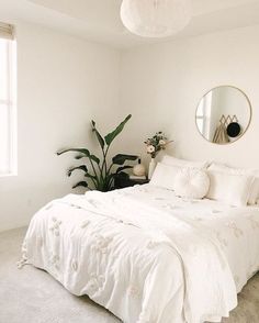 a bedroom with white bedding and plants in the corner