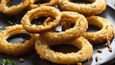 fried onion rings on a black plate with parsley sprinkled around them and seasoning