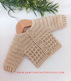 a crocheted sweater and wooden hanger on a white surface with greenery