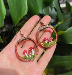 a person is holding two hoop earrings with mushrooms on them in front of some plants