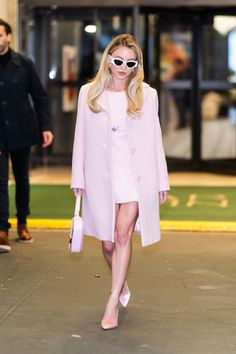 a woman in pink coat and sunglasses walking down the street