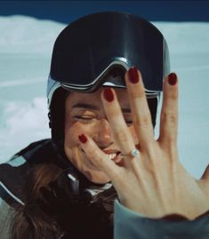 a woman with her hand up to her face and wearing a ski goggles on top of her head