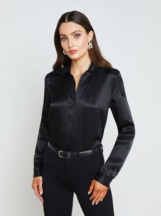 A quintessential blouse in a lustrous silk charmeuse and true black hue. Classic look has a soft, liquid hand and tailored silhouette shaped by sharp sartorial details like a stand collar, long button-cuff sleeves, and back yoke with inverted pleat. An open neckline and curved hem add subtle femininity. A nimble style that works equally well with jeans or skirts. Fastens in front with tonal buttons. | L'AGENCE Tyler Silk Blouse Top In Black