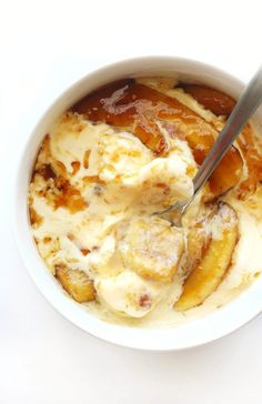 a bowl filled with bananas and ice cream on top of a white table next to a spoon