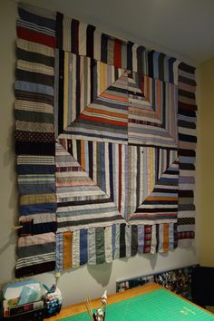 a wall hanging made out of strips of fabric with scissors on the table next to it