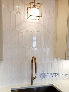 a kitchen sink under a light fixture in a white tiled wall with hexagonal tiles