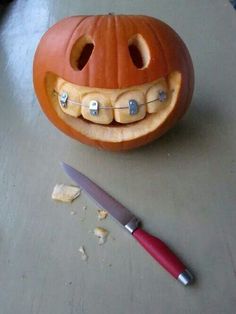 a carved pumpkin with teeth on it next to a knife