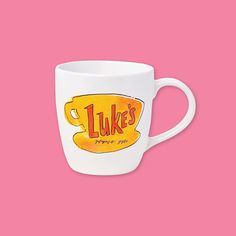 a white coffee mug with the words luke's on it against a pink background