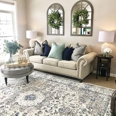 a living room filled with furniture and two large mirrors on the wall above it's windows