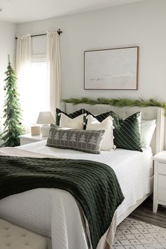 a white bed topped with pillows and blankets next to a christmas tree in a bedroom