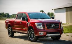 a red truck is parked in front of a white building and some grass on the side of the road