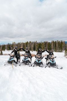 four people on snowmobiles standing in the snow with their arms around each other