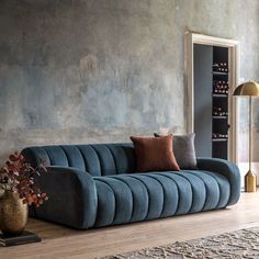 a blue couch sitting on top of a wooden floor next to a vase with flowers