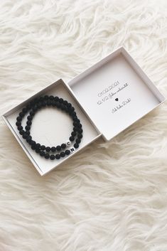 the black beaded bracelet is in a box on a white furnishing surface