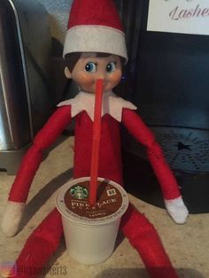 an elf with a straw in his mouth sitting next to a cup of starbucks coffee