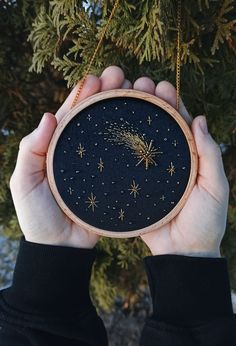 someone holding up a cross stitch ornament in front of a tree with stars on it