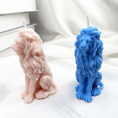 two blue and pink lion candles sitting next to each other on a white bed sheet