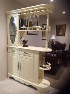 a white bar with wine glasses on it in the corner of a room next to a leather chair