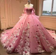 a pink ball gown with white flowers on the skirt is displayed in front of a window