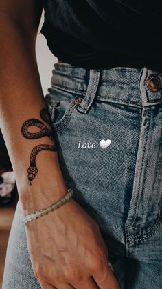 a woman's arm with a snake tattoo on her left wrist and the word love written in white ink