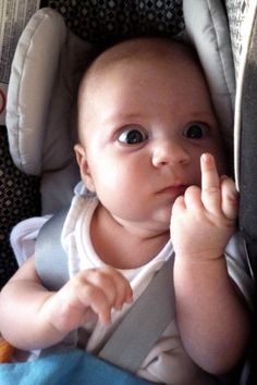 a baby sitting in a car seat with his hand up to the side and looking at the camera