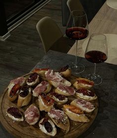 a wooden platter filled with food next to two wine glasses