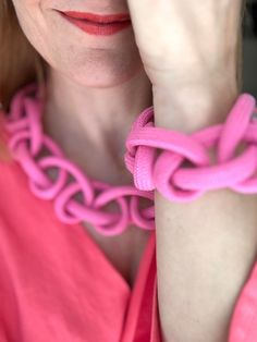 a woman wearing a pink dress holding her hand to her face with a chain around her neck