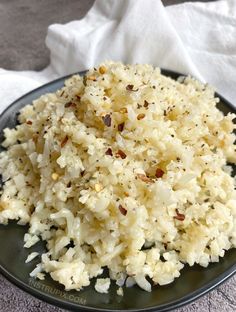 a black plate topped with rice on top of a white cloth covered table next to a napkin