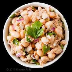 a white bowl filled with lots of food on top of a black table next to a spoon