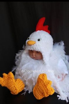 a baby wearing a white chicken costume with red headbands and yellow feet sitting on a black surface