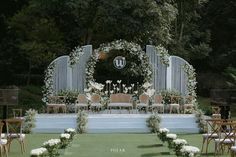 an outdoor ceremony setup with white flowers and greenery on the stage, surrounded by wooden chairs