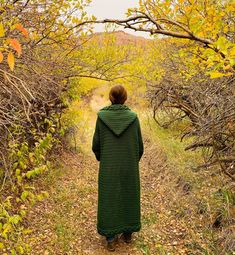 a woman in a green coat is walking down a path through some trees and bushes