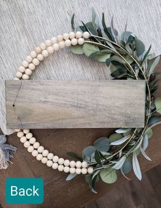 a white beaded necklace with green leaves on it and a wooden sign that says back