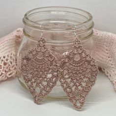 a pair of pink lace earrings sitting on top of a jar next to a scarf