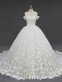 a white wedding dress with flowers on the skirt and off - the - shoulder neckline