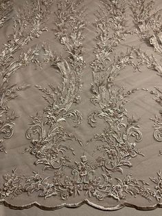 an embroidered fabric with silver flowers and leaves on the side, along with white thread