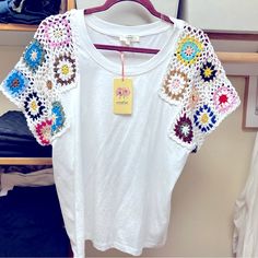 a white t - shirt with crocheted details hanging on a rack