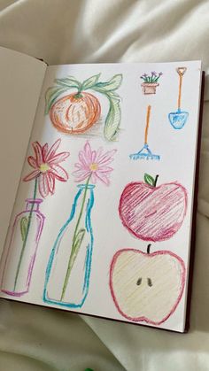 an open notebook with drawings of apples, flowers and vases on the cover is laying on a bed