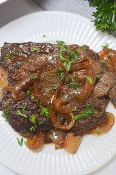 a white plate topped with meat and onions on top of a wooden table next to parsley