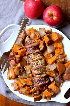 a white plate topped with meat and veggies next to two apples on top of a wooden table