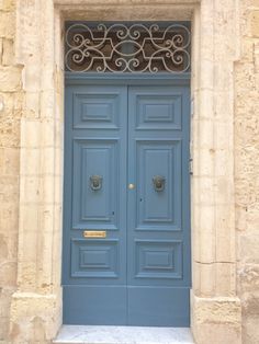 a blue door with ornate iron work on the top and bottom, in front of a stone building